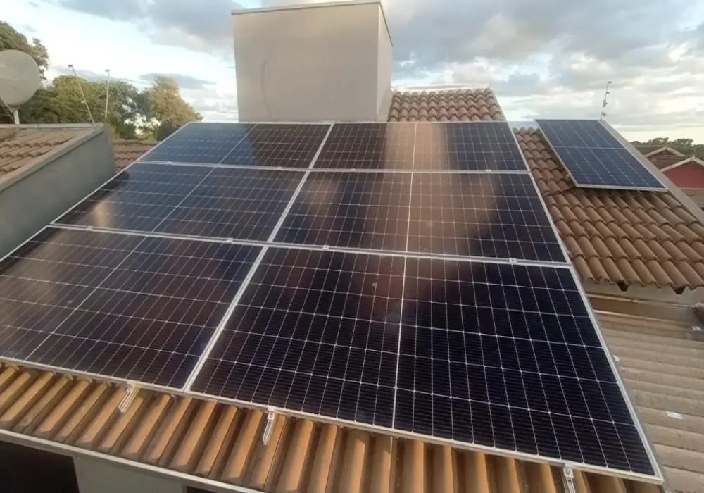 Painéis solares instalados em um telhado de telhas em uma área residencial, com céu parcialmente nublado ao fundo